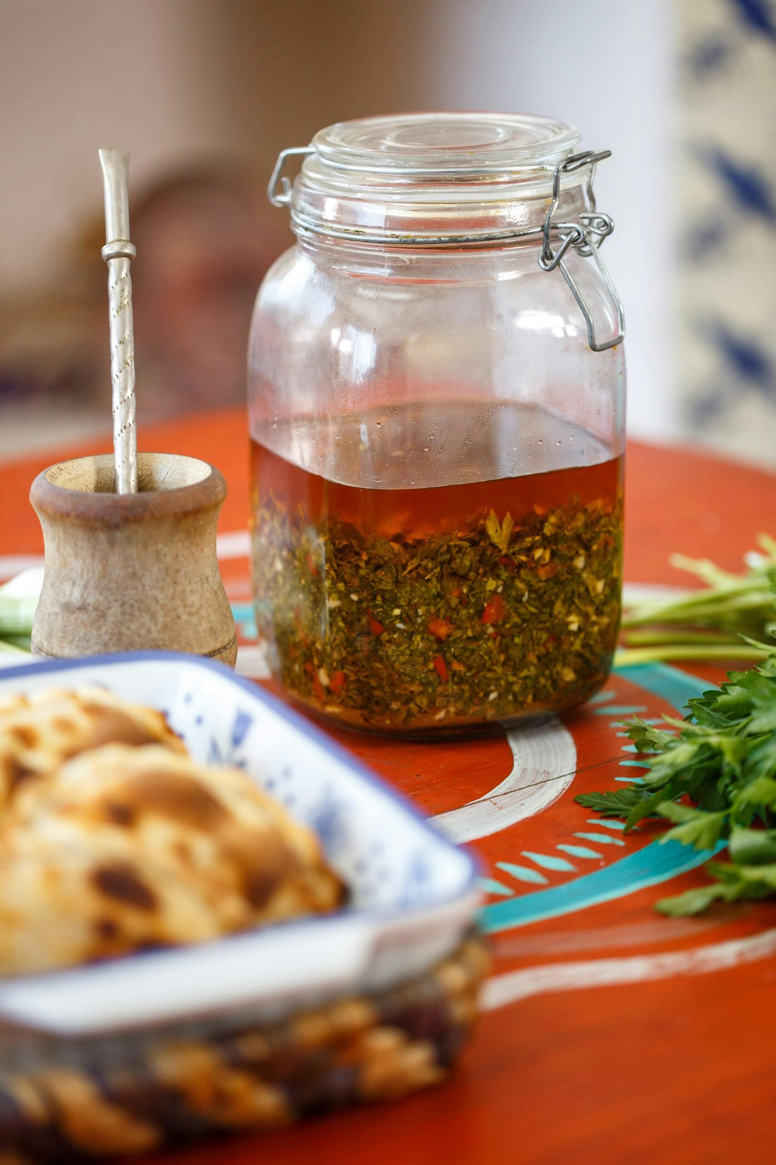 A close-up of traditional chimichurri sauce in a jar beside mate cup on a vibrant table setting.