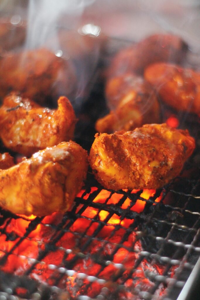 Close-up of sizzling tandoori chicken pieces on a hot grill, showcasing vibrant spices and smoky flavors.